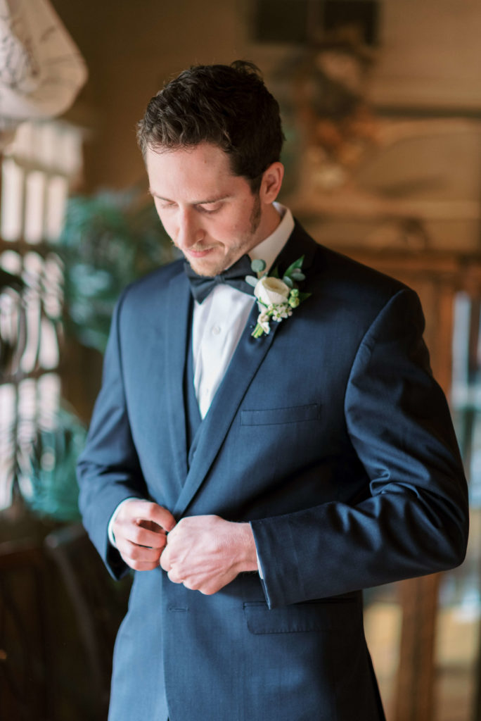 Groom in navy suit buttoning up jacket while getting ready