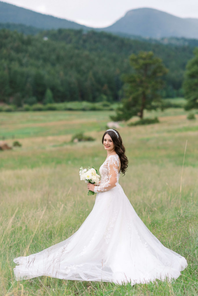 Bride in white lace dress standing in field and looking into the camera
