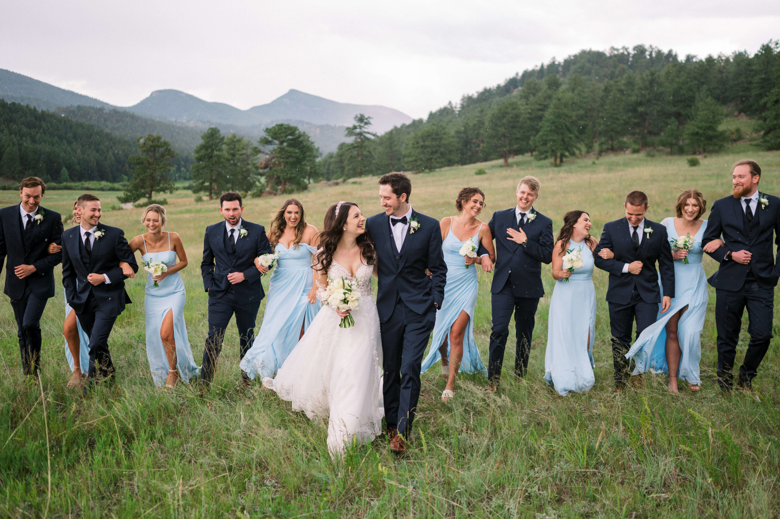 Bride, Groom, and Bridal party walking in a field with mountains in the background at wedding planned by Privé events