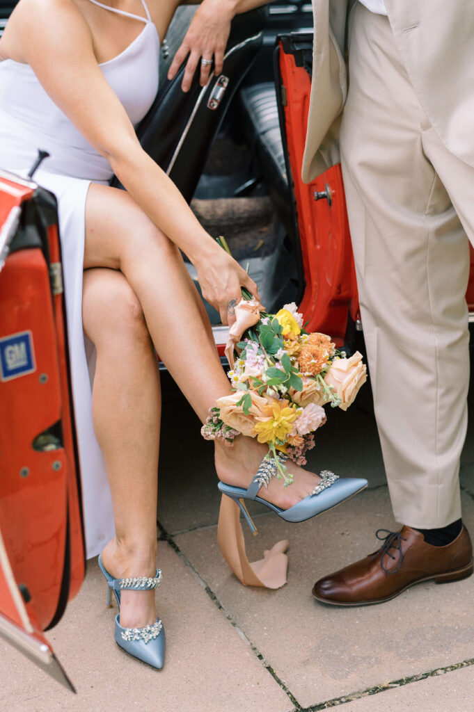 Stylish shoes on a bride and groom while they pose with their vintage car