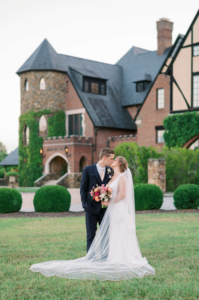 While standing in front of Dover Hall Estate, a bride and groom passionately kiss after their wedding