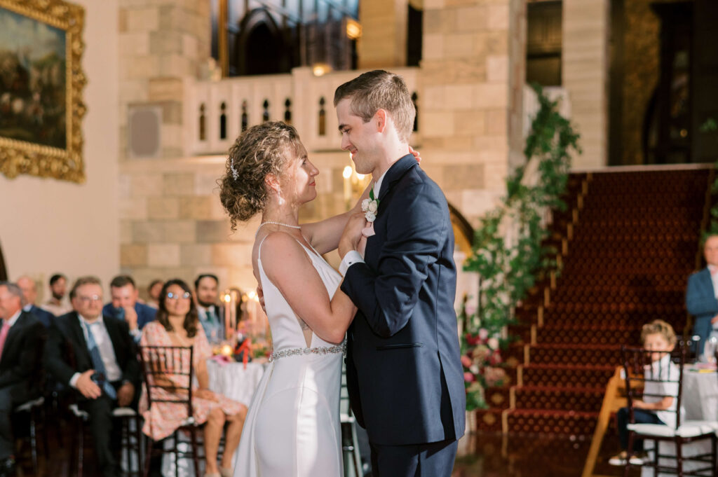 Bride in white dress holds the hand of her husband in a navy suit while they enjoy their first dance together