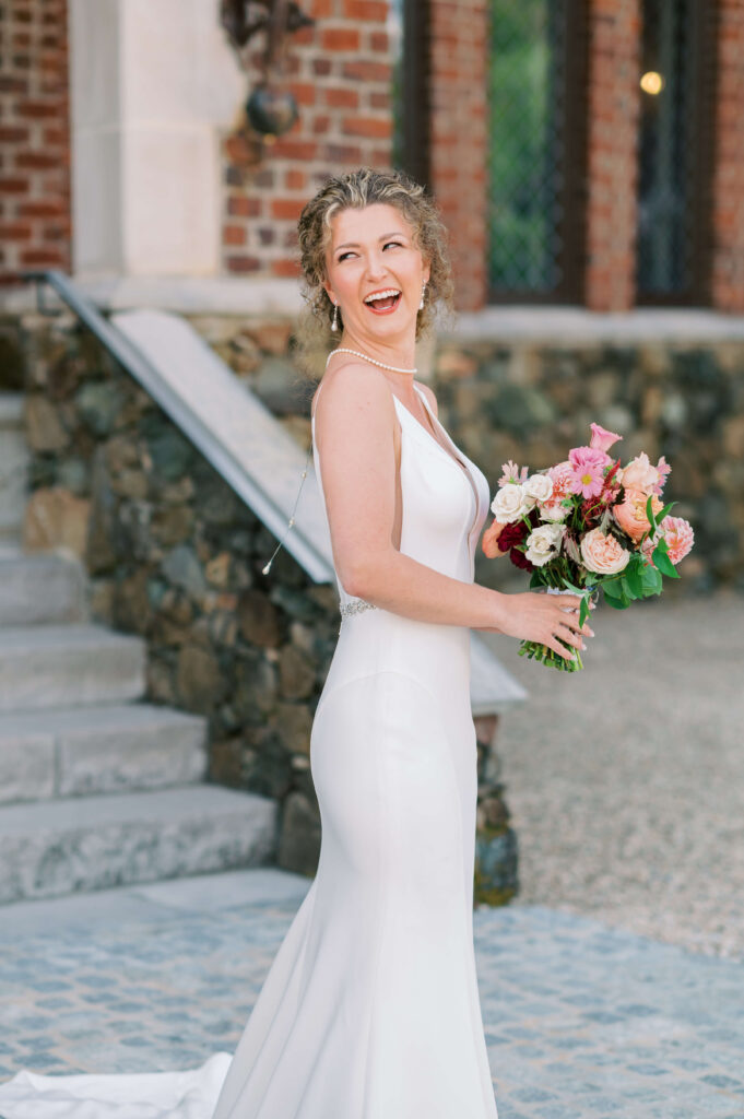 Bride laughs at her new husband while looking over her shoulder and holding a blush bouquet