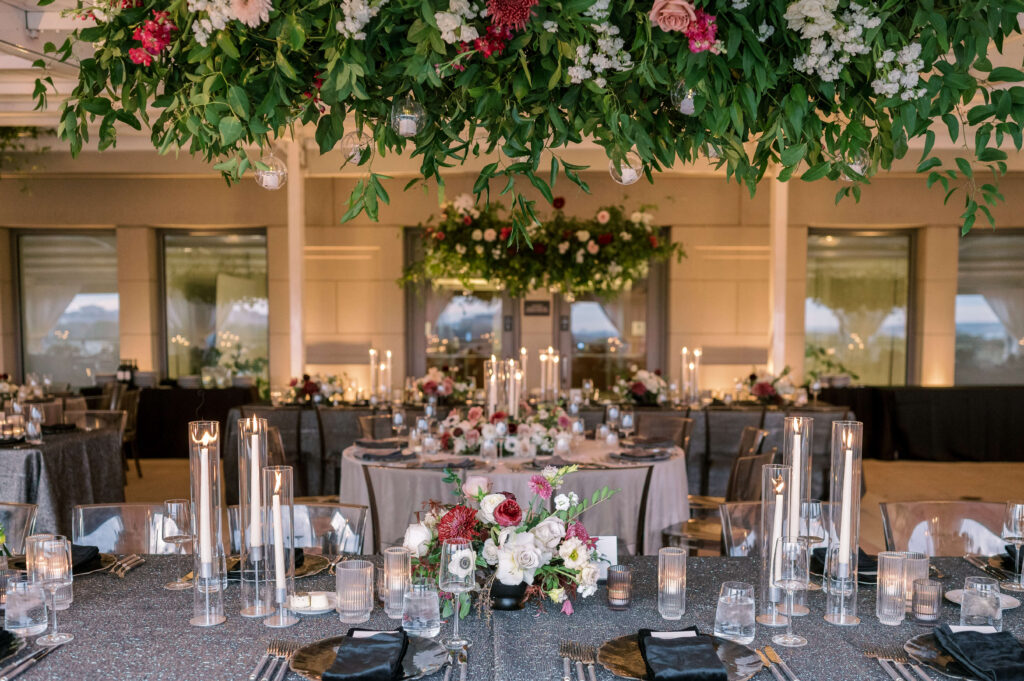 pink and white flowers adorn tables covered with grey tablecloths and plenty of candles during a covered outdoor reception